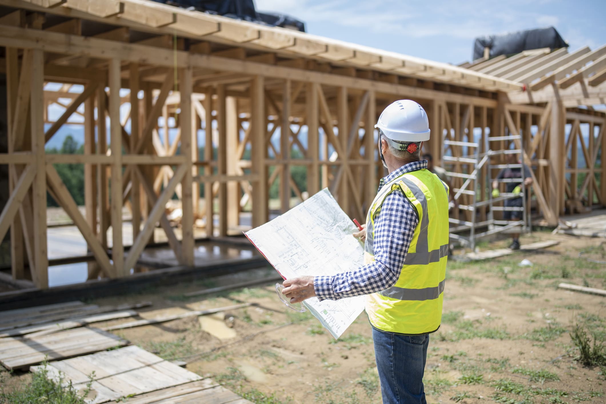 A shot of a confident man wearing reflective vest and helmet , holding a building plan and looking at the construction side.