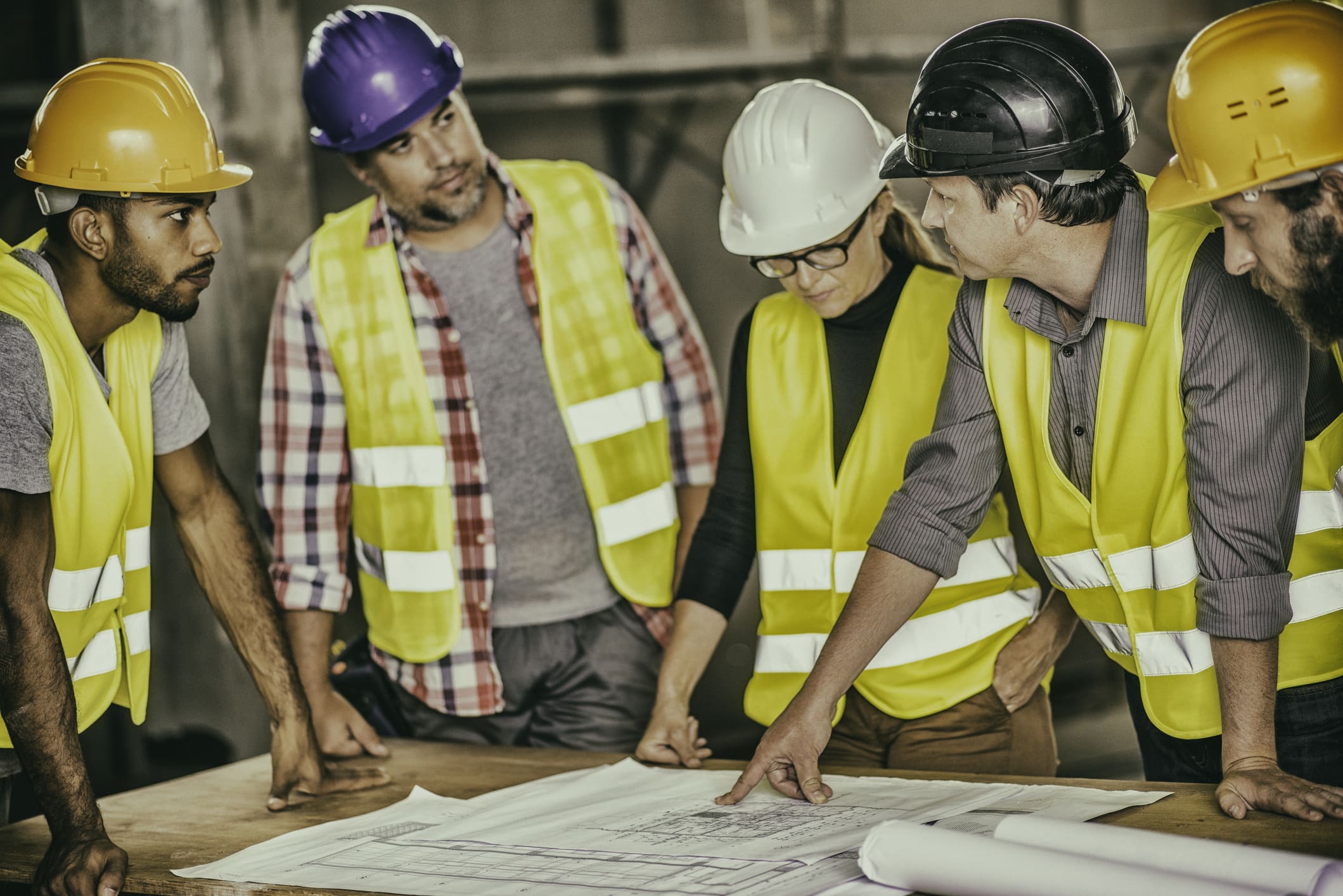 Construction engineer consulting female architect, construction foreman and construction workers about blueprints.